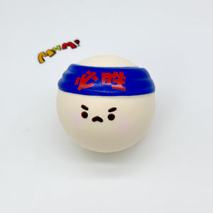 Single white round squishy toy with blue Chinese headband, grumpy face detail, white background close-up