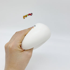 Hand gripping white chubby bird squishy toy sideways, showing soft slow-rise texture and cute face