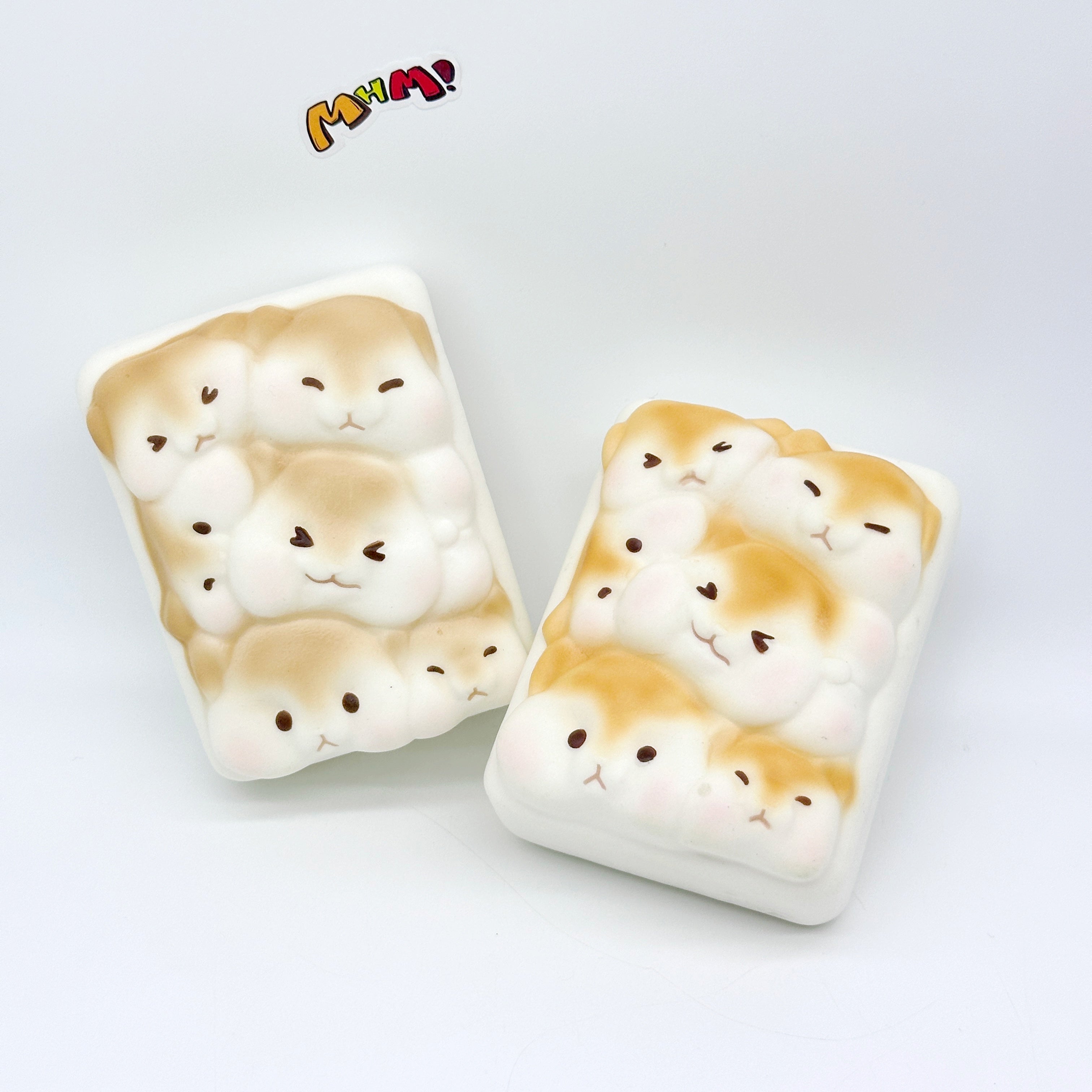 Two cute hamster toast slow rise squishy toys side by side, white foam with golden brown markings